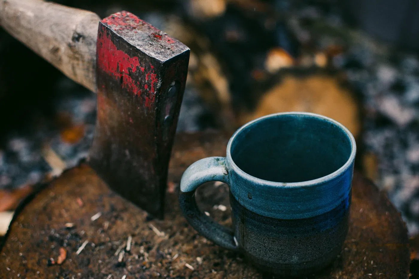 The enamel mug in slate, standing on a chopping block outdoors.