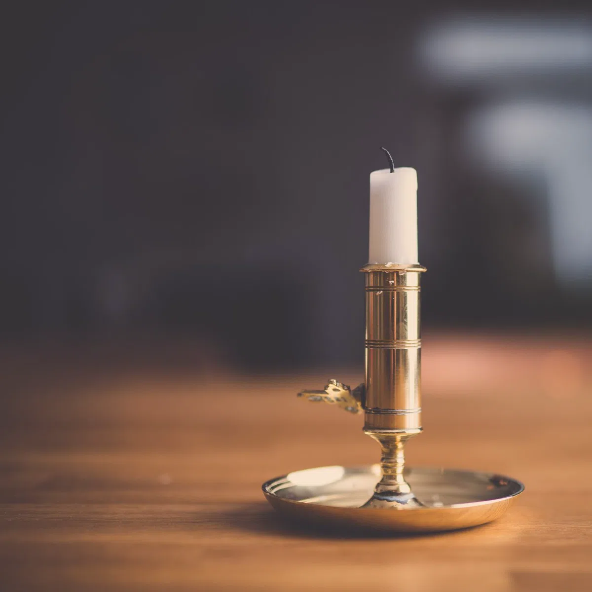 A beeswax candle in a brass holder, unlit.
