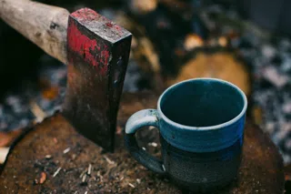 The enamel mug in slate, standing on a chopping block outdoors.