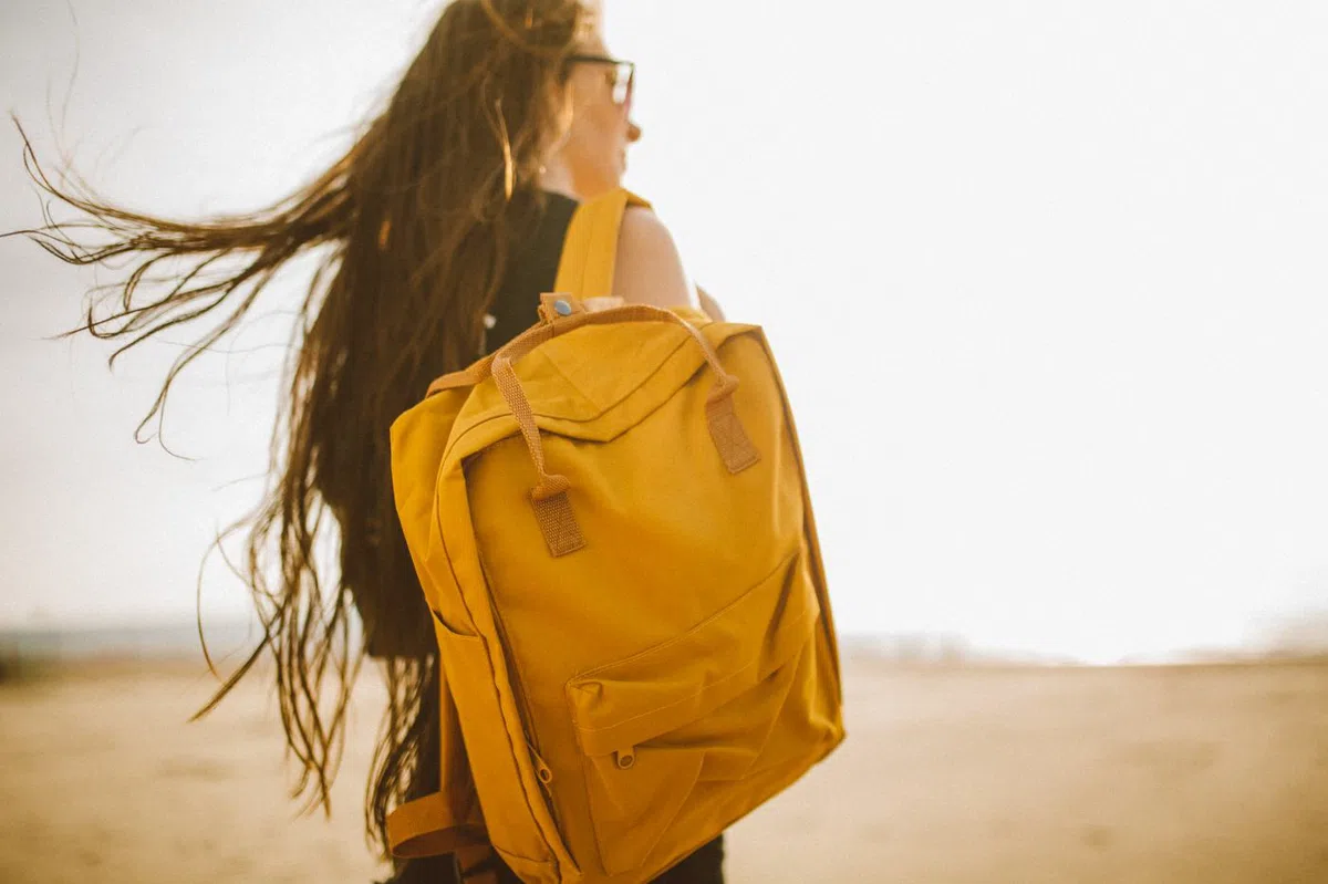 The canvas backpack in ochre, carried on one shoulder.